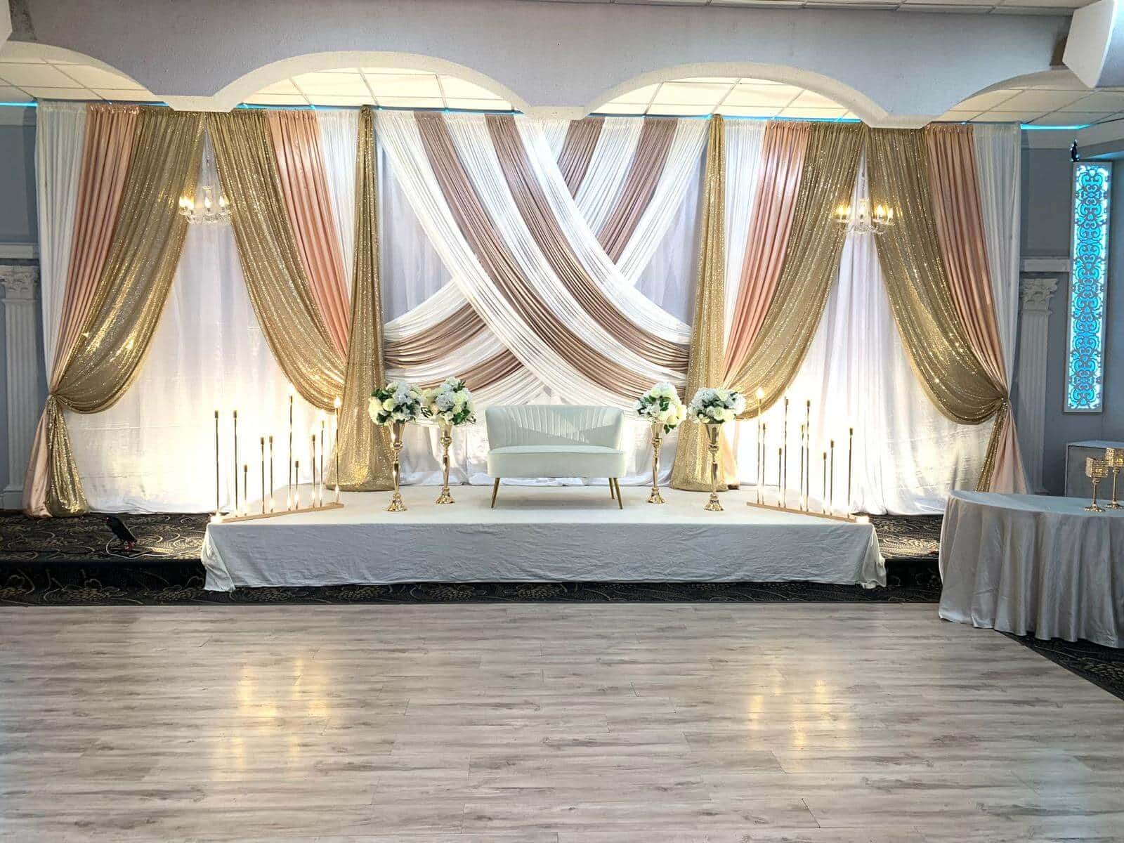 The Grand Ballroom stage dressed in white and gold drapery, framed by floral arrangements and set for a wedding reception.