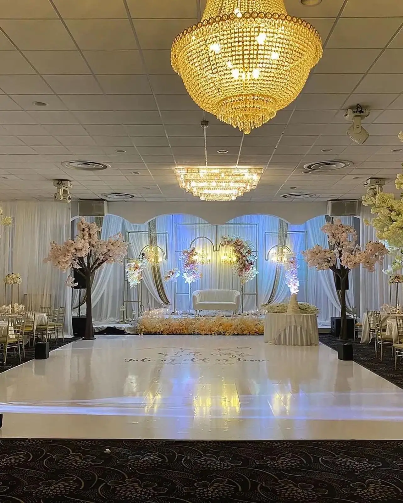 Stage backdrop of white florals behind a low couch for the wedding party.