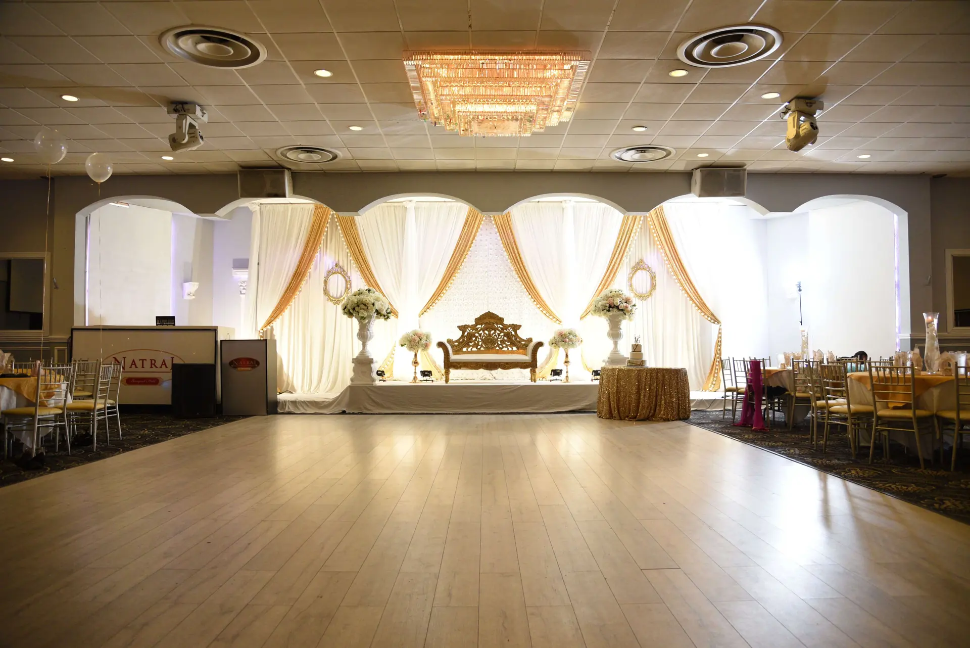 Wedding stage with a gold backdrop and upholstered seating for the couple.